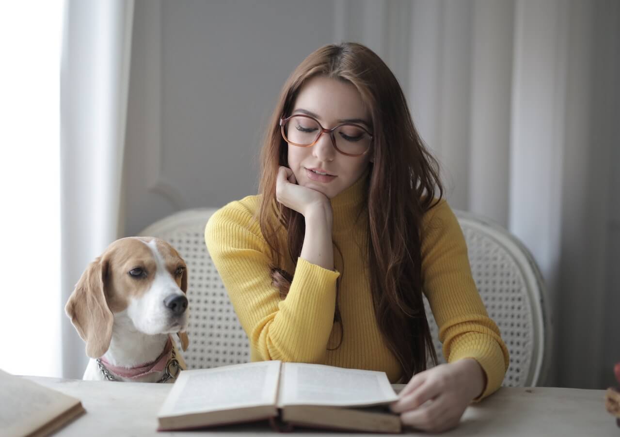 woman reads book as beagle watches
