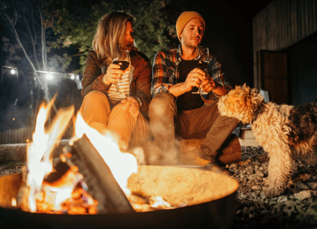 a couple and their dog enjoy a bonfire, wine, and other treats